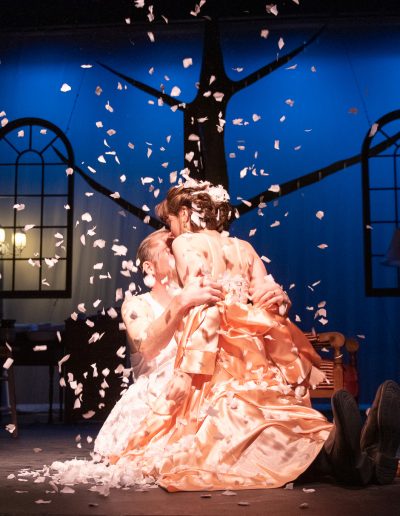 Two performers embrace each other under falling snow